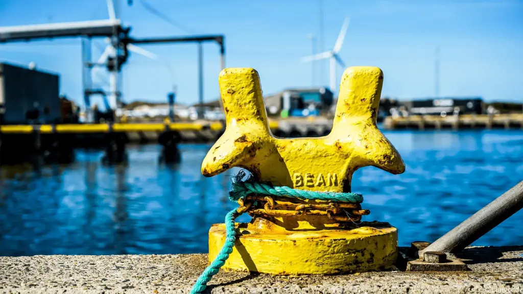Gelber Poller an einer Werft mit Wasser und Hafen im Hintergrund